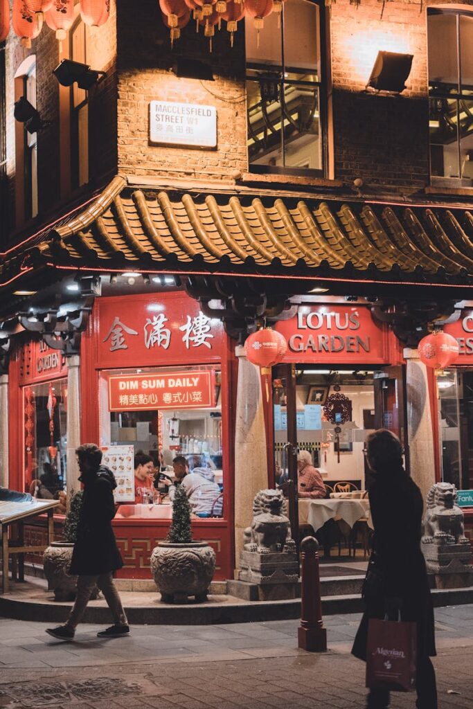 A vibrant night scene of lively Chinatown in London, featuring a traditional Chinese restaurant illuminated by red lanterns.